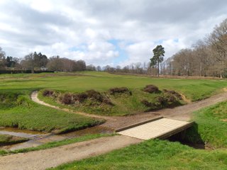 View back across a golf course with a bridge in the foreground crossing a small river
